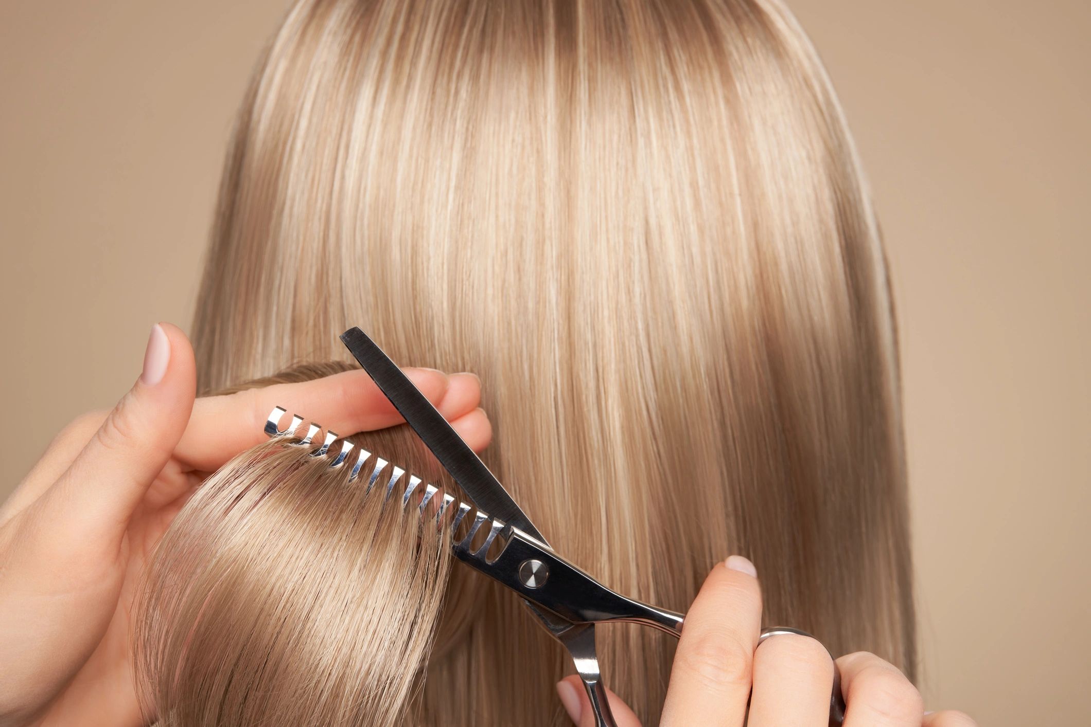 Hairdresser skillfully trimming long blonde hair, showing expert technique.